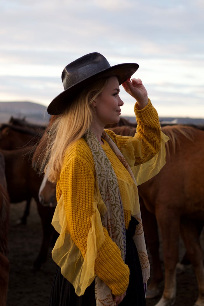 services-04 Blonde woman in a rural setting with horses, wearing a wide-brim hat, exemplifying cowgirl style.